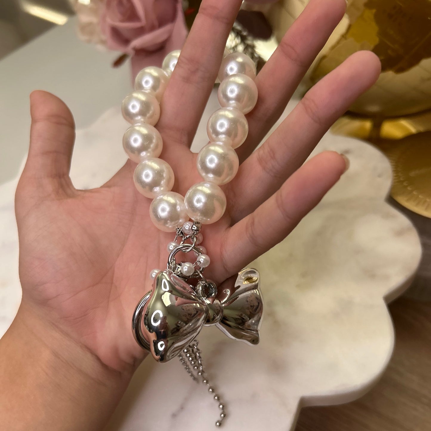 Hand holding a pearl bracelet with a silver charm against a blurred background