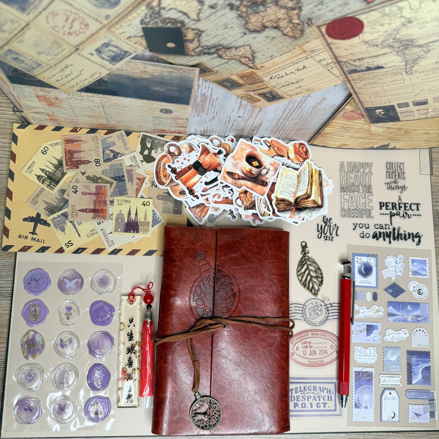 Collection of stationery items including a leather notebook, stickers, and a world map on a wooden surface.