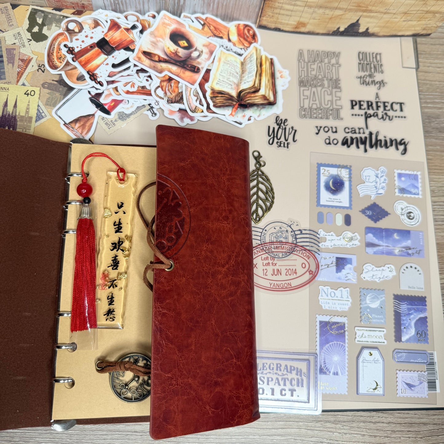 Collection of decorative items including a leather-bound book, stickers, and a pen holder on a textured surface.