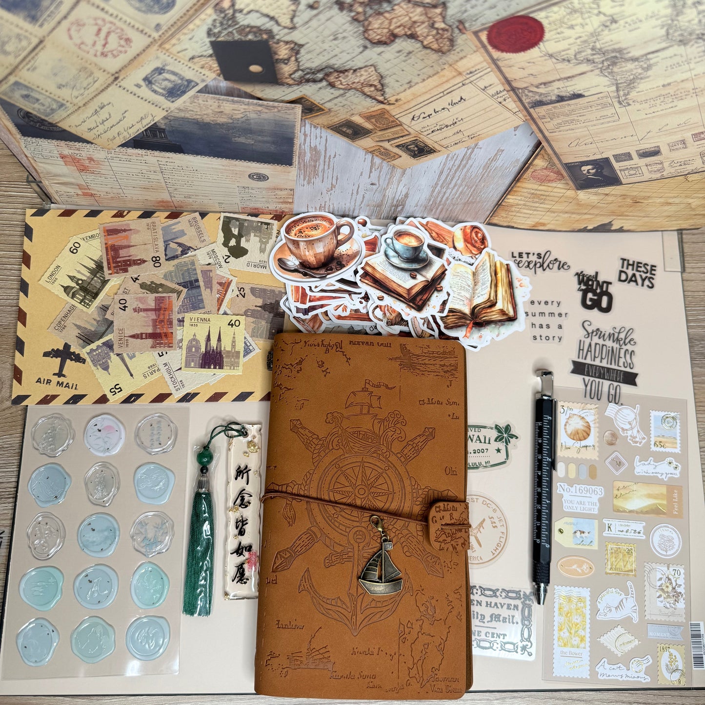 Collection of stationery items including a brown leather notebook, stickers, and a world map on a wooden surface.
