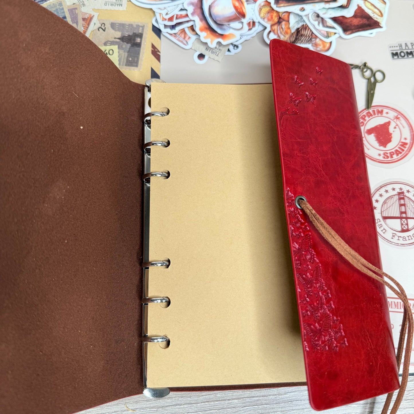 Open notebook with a red leather cover and decorative stickers on a wooden surface