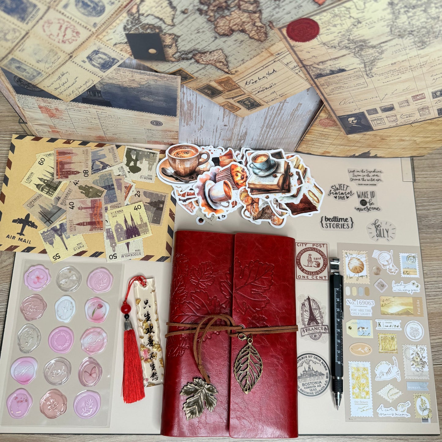 Collection of vintage-style stationery items including a red leather notebook, stickers, and maps on a wooden surface.