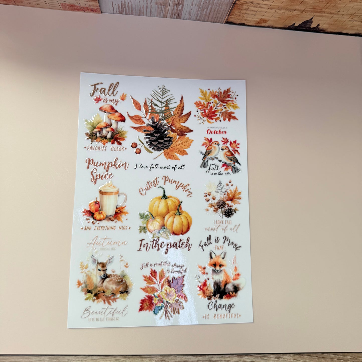 Sheet of fall-themed stickers with pumpkins, leaves, and text on a wooden surface.