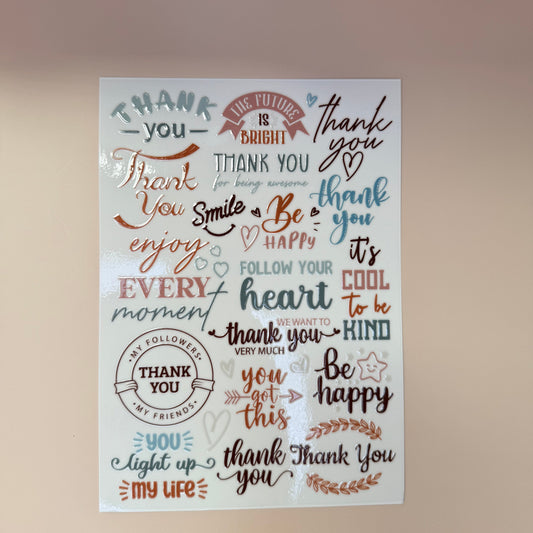 Sheet of decorative stickers with various phrases and designs on a wooden surface.
