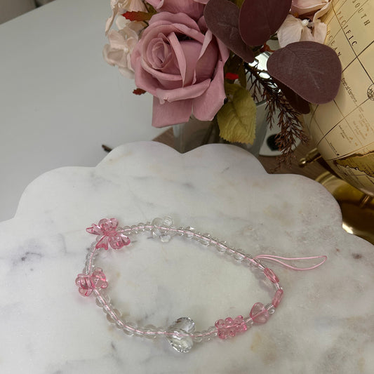 Pink beaded necklace with floral designs on a marble surface with flowers in the background