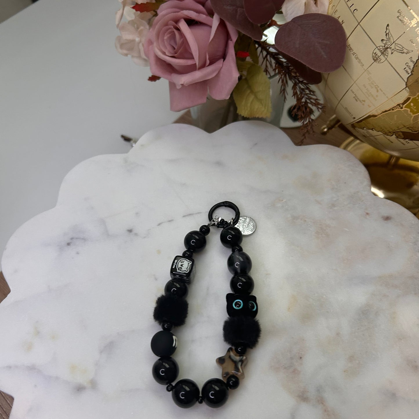Black beaded bracelet on a marble surface with pink flowers in the background