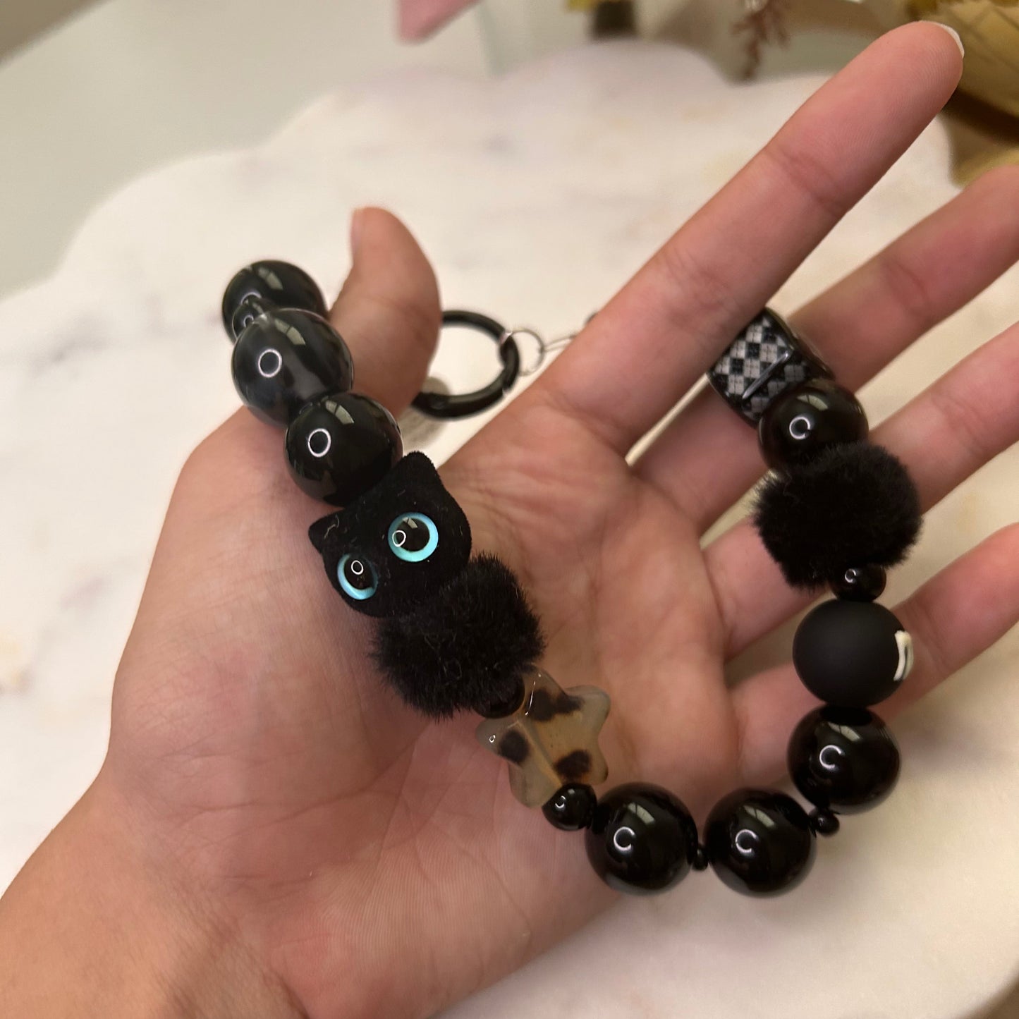 Black beaded bracelet with small plush toys held in a hand against a neutral background