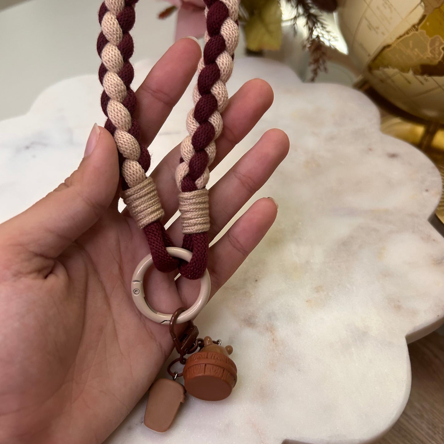 Hand holding a braided keychain with a decorative item in the background