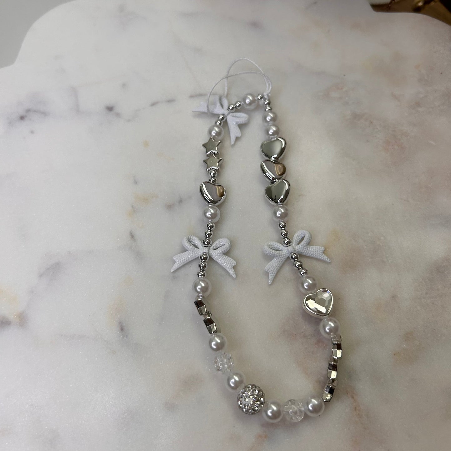 Silver bracelet with heart and bow designs on a marble surface
