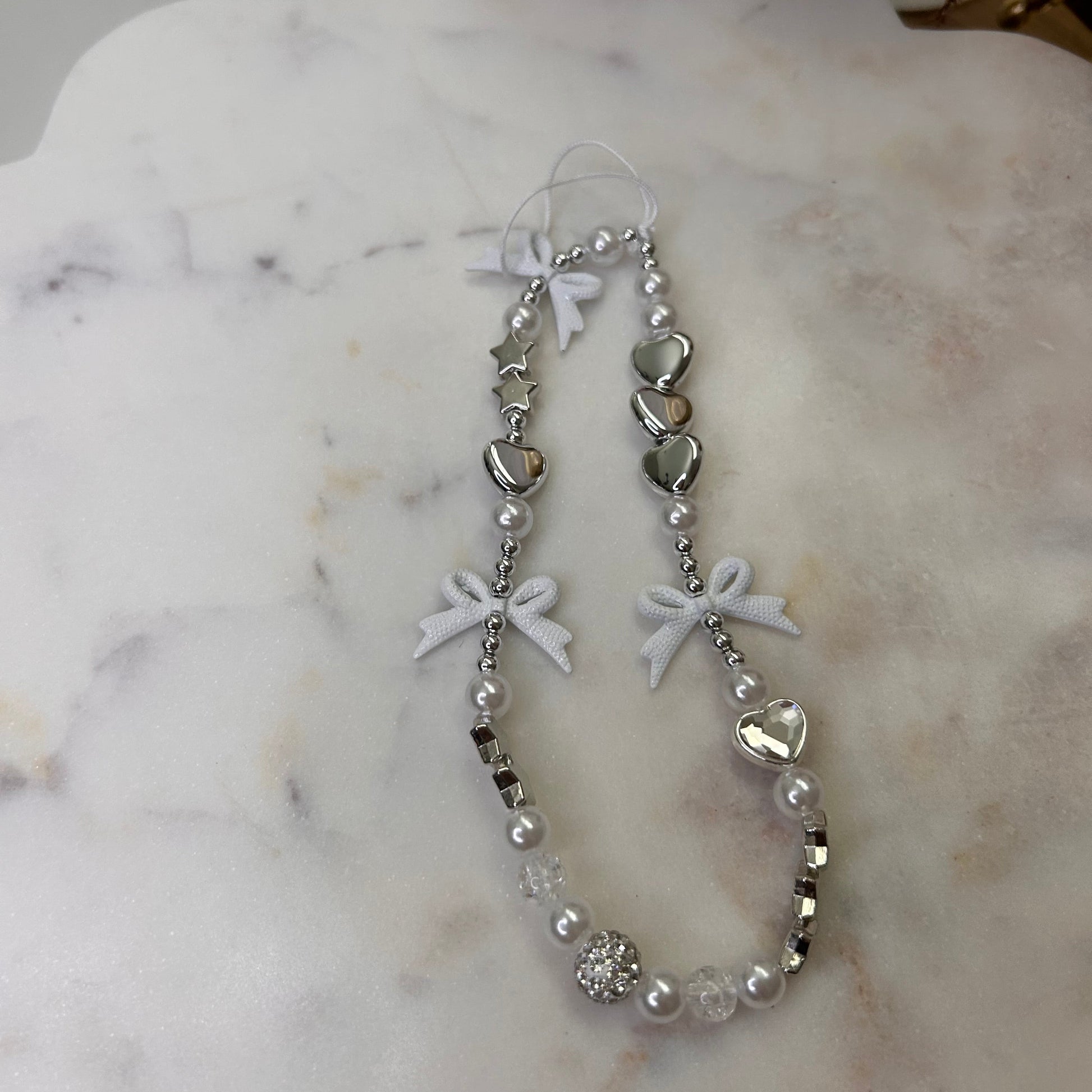 Silver bracelet with heart and bow designs on a marble surface