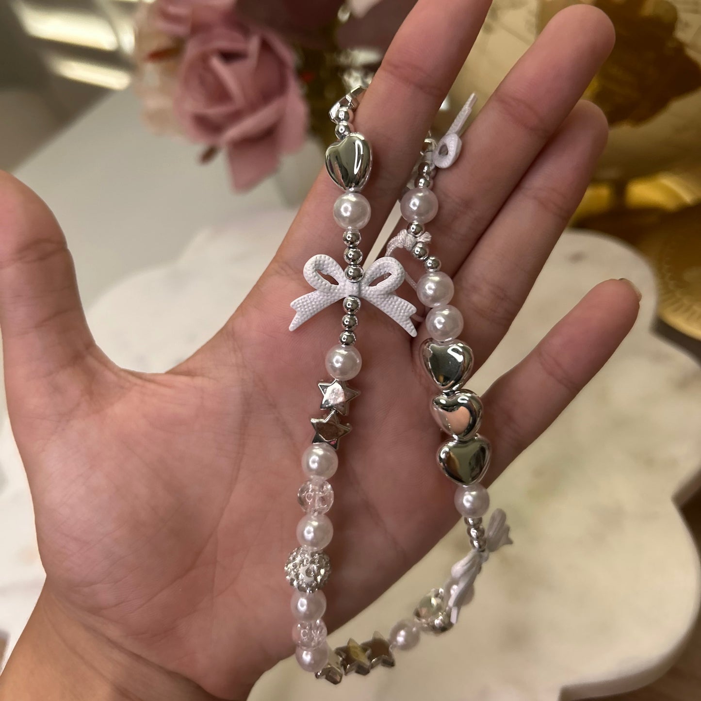 Hand holding a beaded bracelet with decorative elements against a blurred floral background