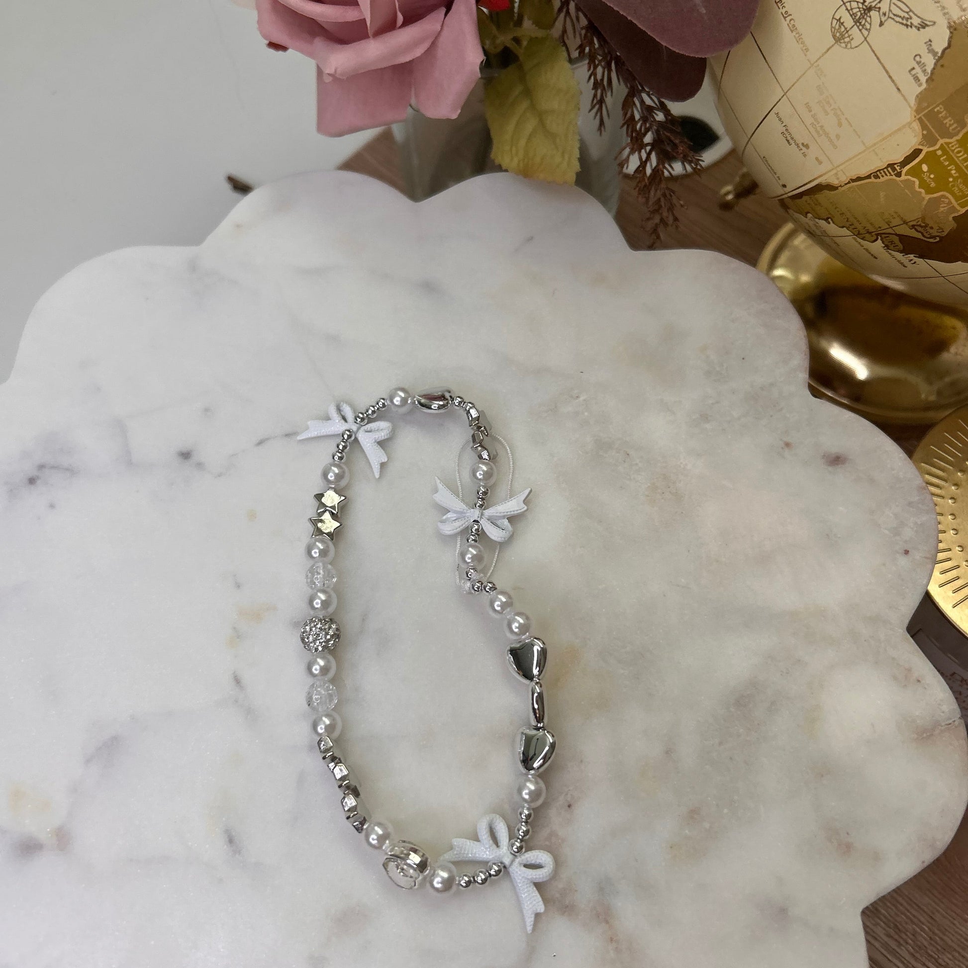Silver bracelet with white flowers on a marble surface with decorative elements.