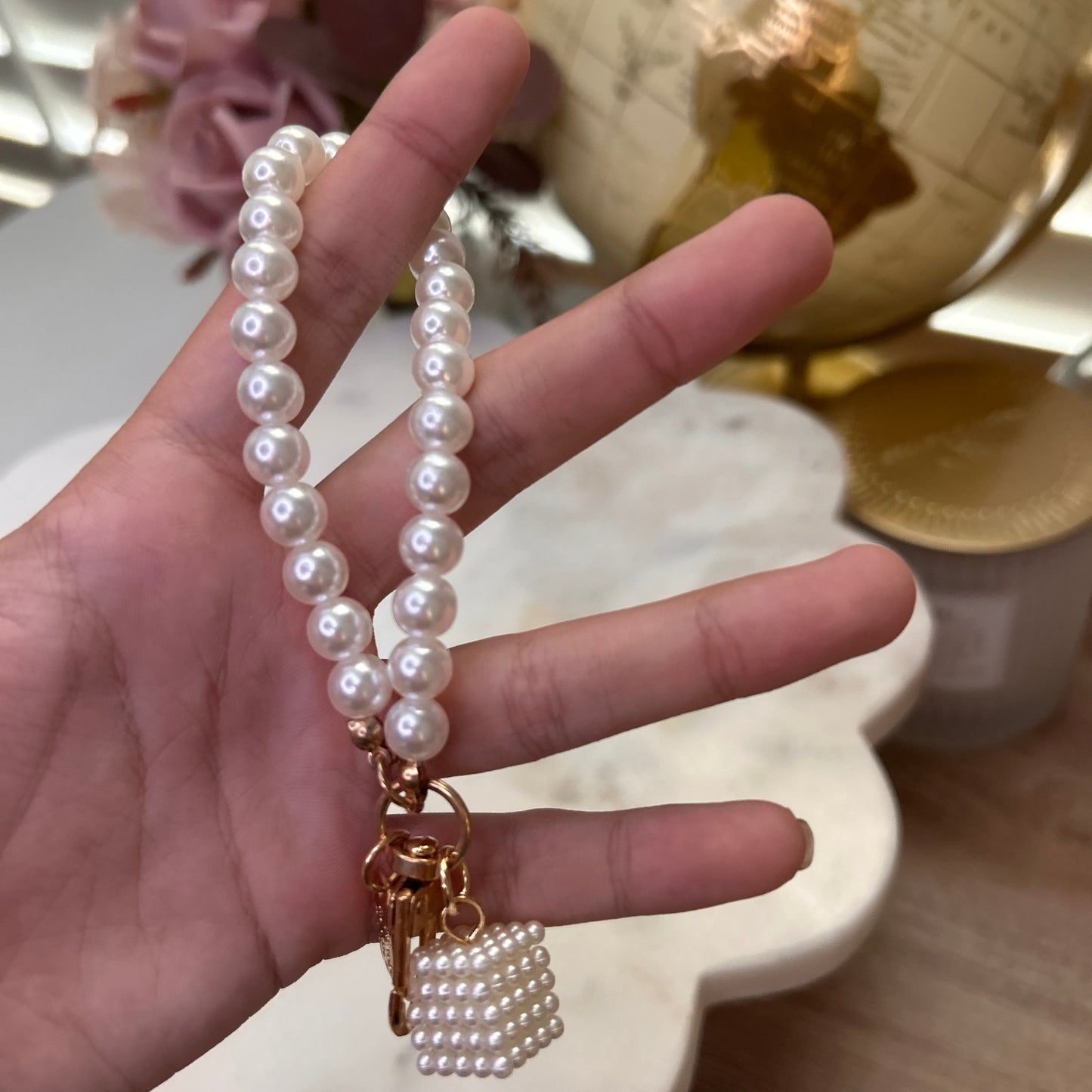 Hand holding a pearl necklace with a gold clasp against a blurred decorative background