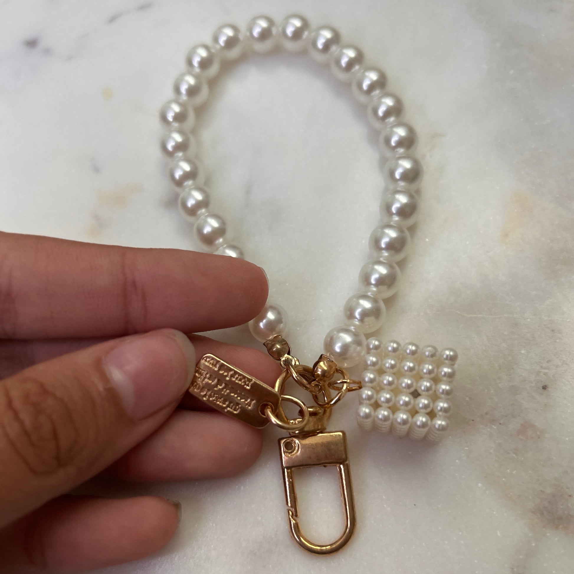 Pearl bracelet with a gold clasp held by a hand on a marble surface