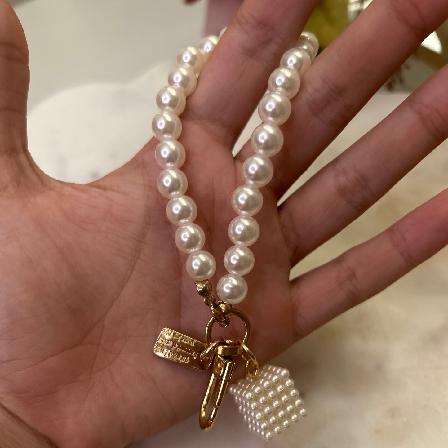 Pearl bracelet with a gold clasp held in a hand on a marble surface