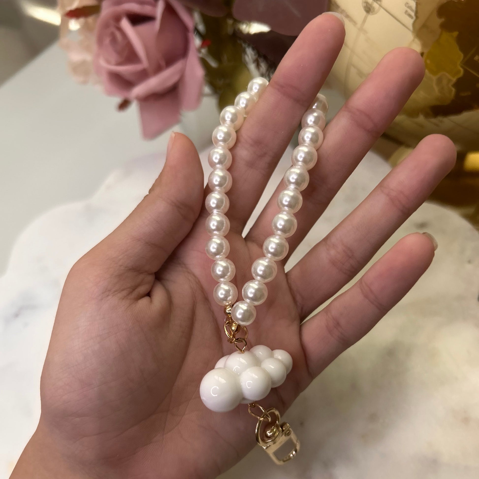 Hand holding a pearl necklace with a cloud charm against a blurred background