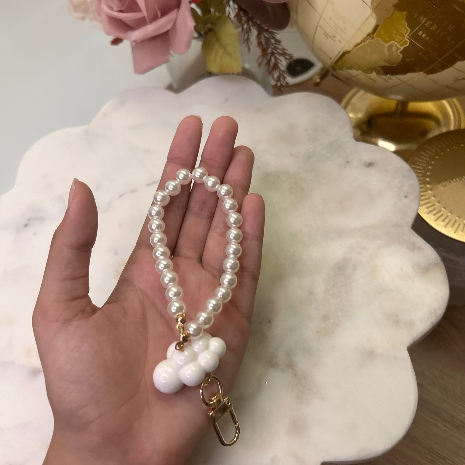 Hand holding a pearl bracelet with a decorative background