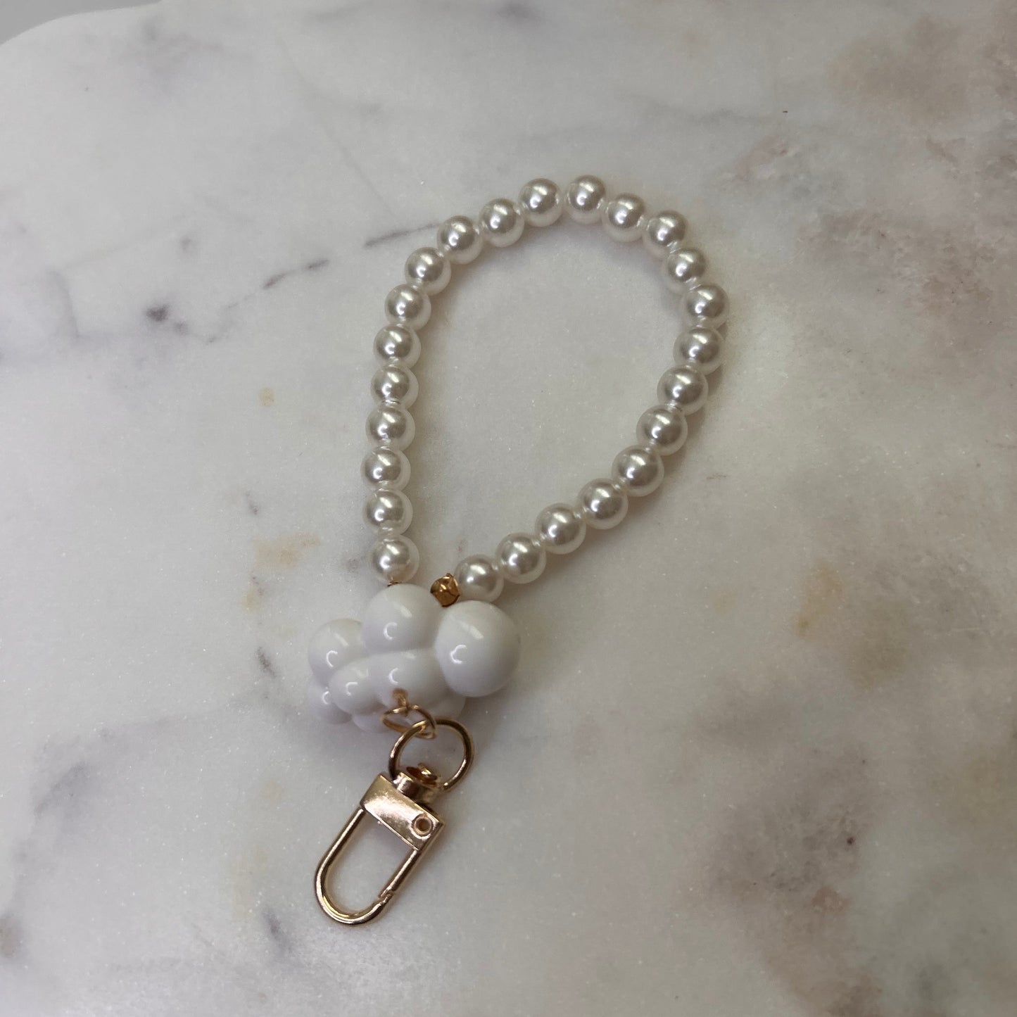 Pearl keychain with a gold clasp on a marble surface