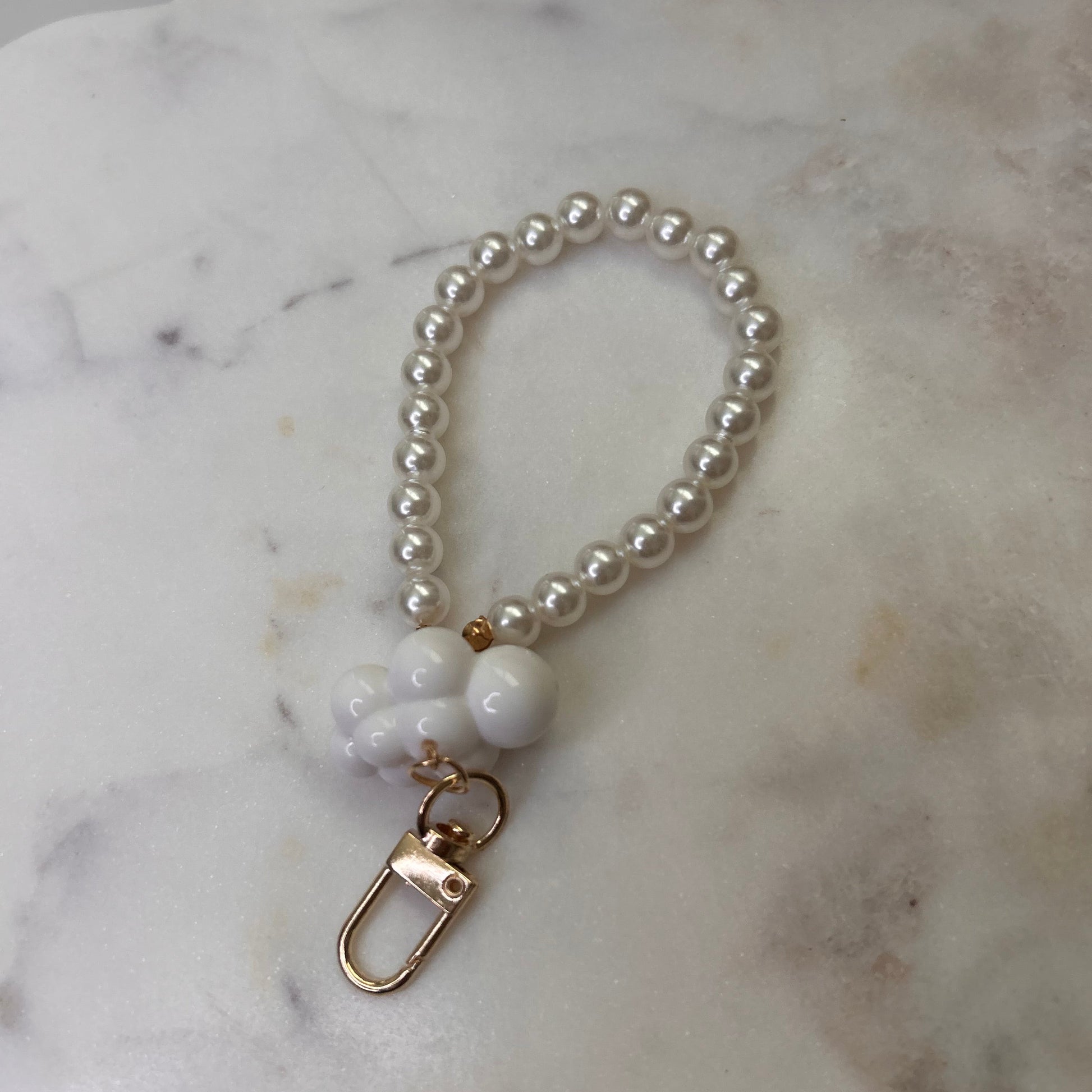 Pearl keychain with a gold clasp on a marble surface