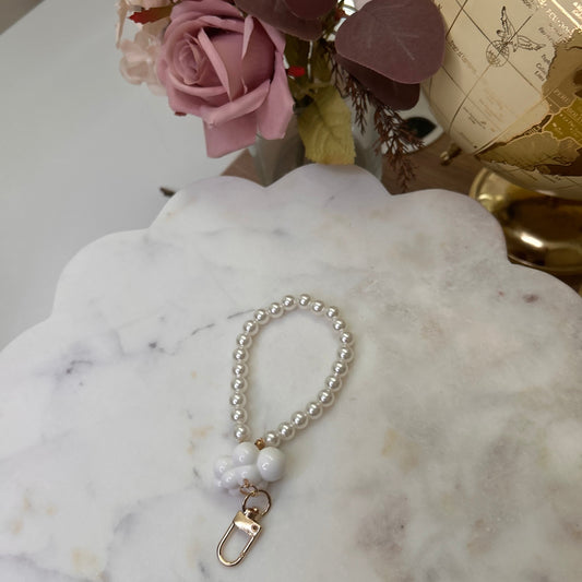 Pearl bracelet with a gold clasp on a marble surface next to pink flowers and a globe.