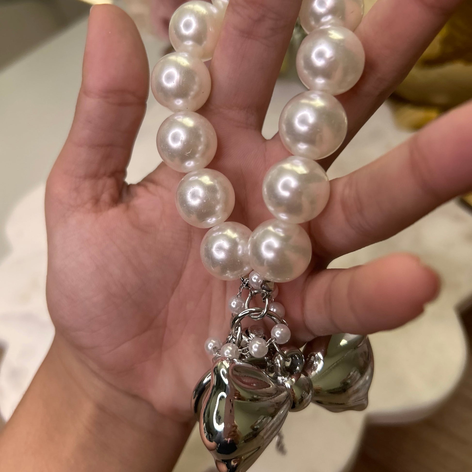 Hand holding a pearl bracelet with a silver clasp against a blurred background