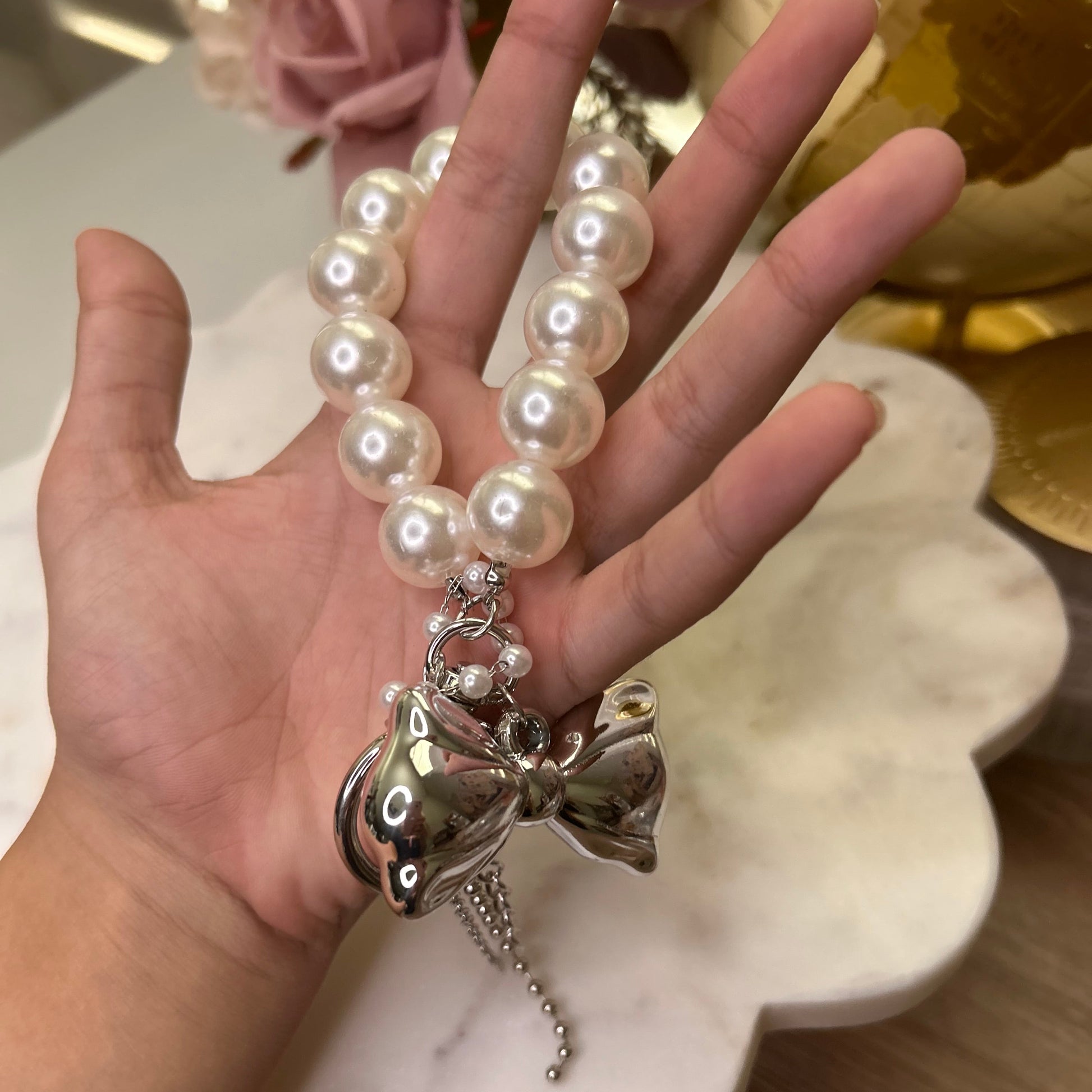 Hand holding a pearl bracelet with a silver charm against a blurred background