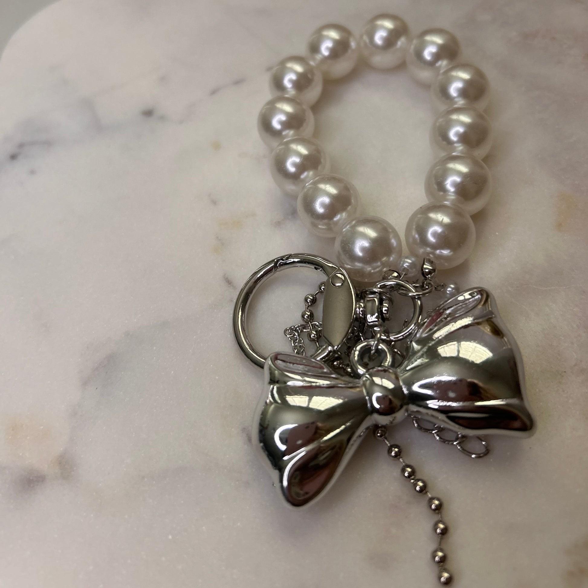 Pearl bracelet with a silver bow charm on a marble surface