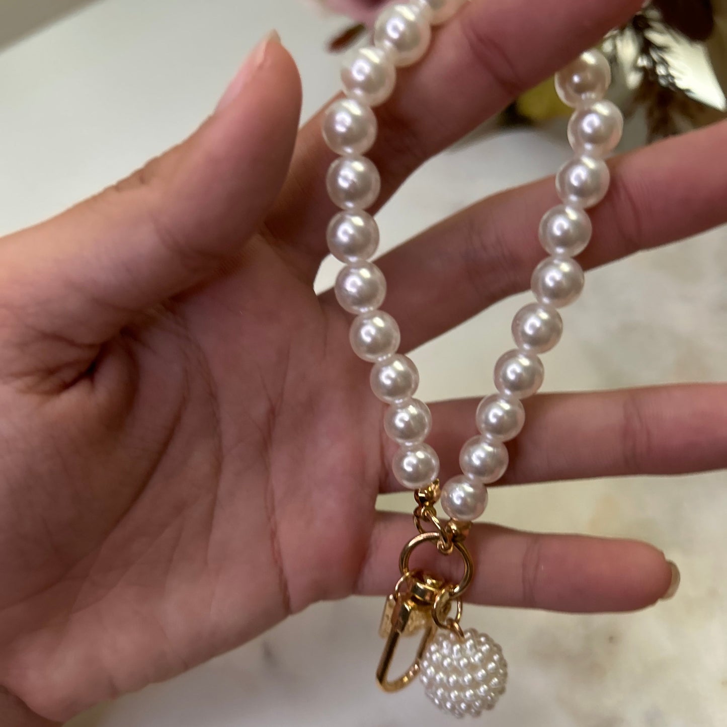 Pearl necklace with a gold clasp held by a hand on a marble surface