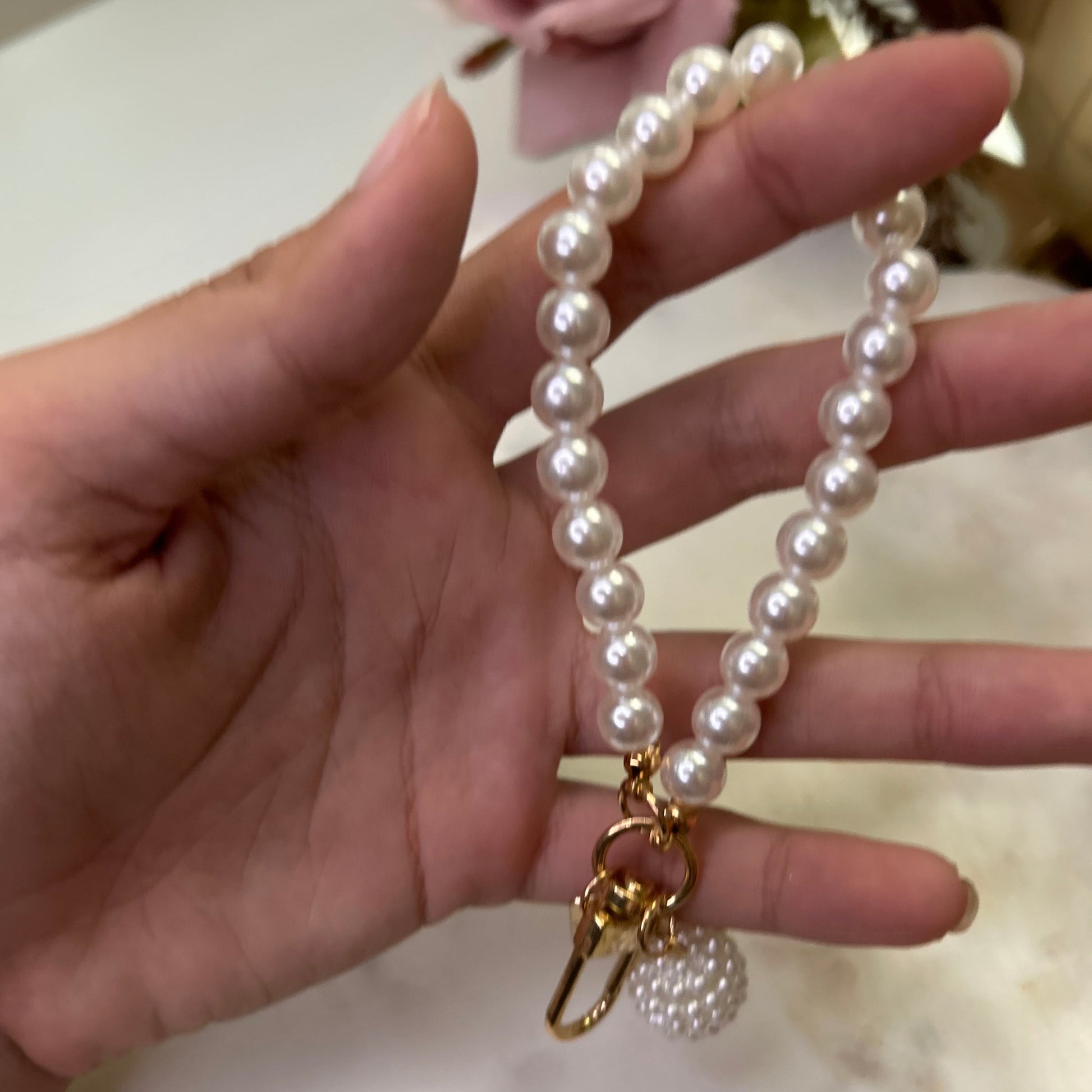 Hand holding a pearl necklace with a gold clasp against a blurred background